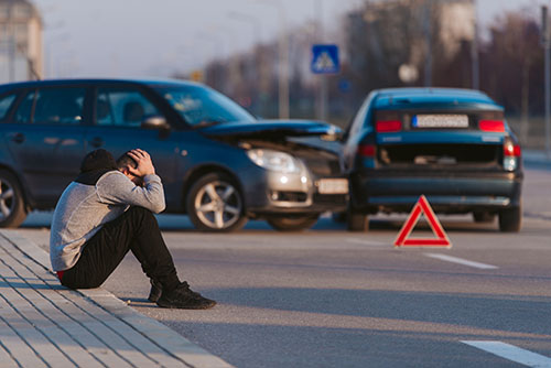 A man is looking sad after two cars crashing on the road. Don't get caught without PIP and Uninsured and Under Insured Motorist coverage